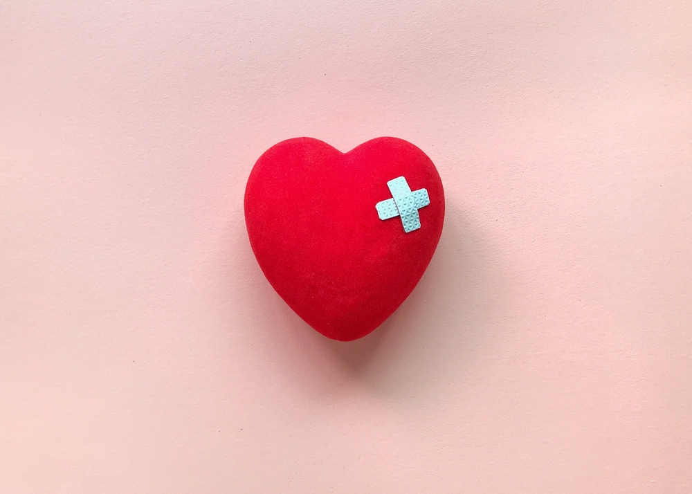 injured red heart on pastel pink background.